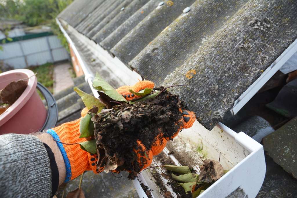 Man scooping out leaves while cleaning gutters in Portland